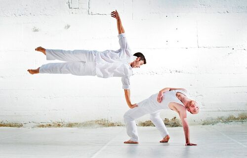Two figures in movement with one airborne with one hand on the other's knee
