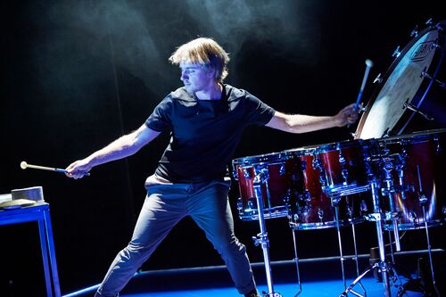 A figure drumming on stage