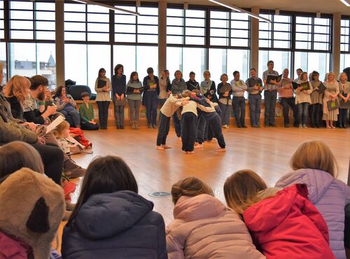 Four figures performing in the middle of a large circle of participants and audience