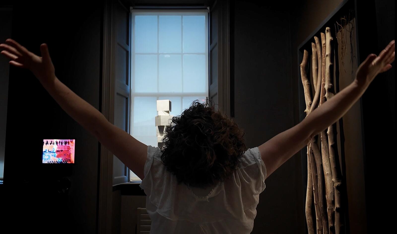 A woman with raised hands facing the window