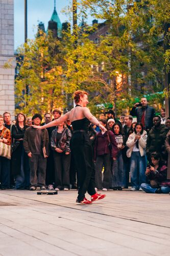 A dancer in a movement with spectators on the background watching outdoor performance