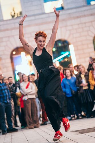 A dancer in a movement with spectators on the background watching outdoor performance