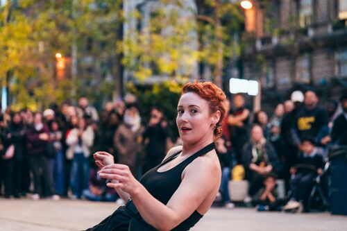 A dancer in a movement with spectators on the background watching outdoor performance