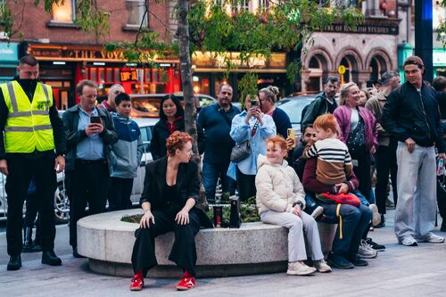 A performer sitting on a bench surrounded by spectators